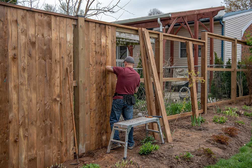 A white, middle-aged gay man builds a wooden fence in his back yard.