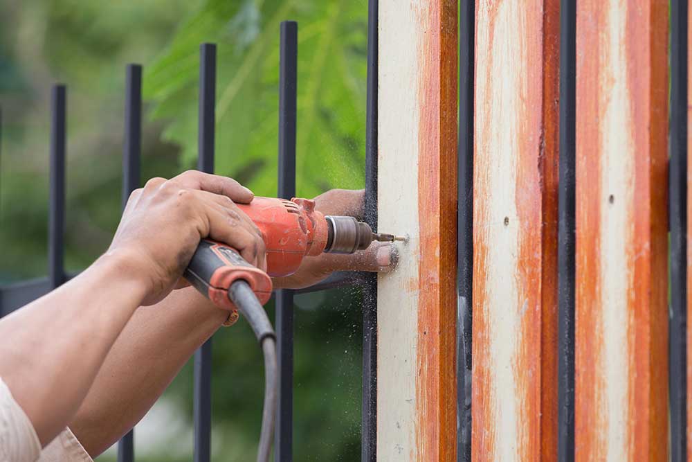 Hands using electric drill on fence wood